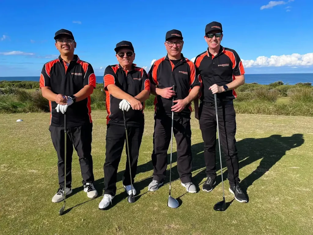 Judi, Emmanuel, Wayne, and Todd on the golf course posing in a line